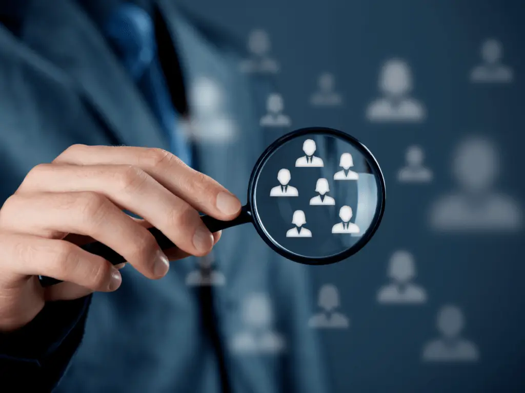 Hand holding a magnifying glass focusing on customer profiles, symbolizing customer segmentation and data analysis for targeted marketing strategies.